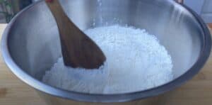 Mixing flour in a stainless steel bowl with a wooden spoon, perfect for baking recipes.